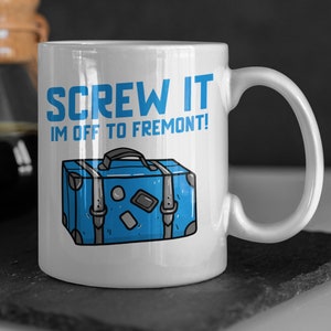 Peut inclure: Une tasse en céramique blanche avec une illustration bleue et noire d'une valise et le texte "SCREW IT IM OFF TO FREMONT!"