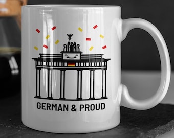 May include: White ceramic mug with a black and white illustration of the Brandenburg Gate, with red and yellow confetti falling. The text "GERMAN & PROUD" is printed below the illustration.