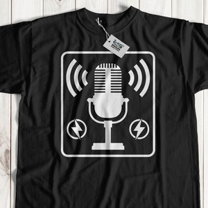 Puede incluir: Camiseta negra con un gráfico blanco de un micrófono dentro de un cuadrado con rayos en cada lado. El gráfico también incluye un icono de señal inalámbrica a cada lado del micrófono.