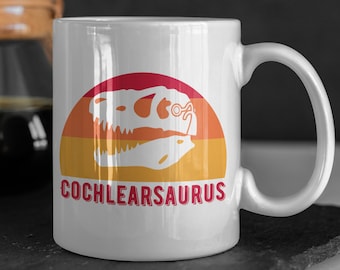 Puede incluir: Taza de café de cerámica blanca con un gráfico retro de un cráneo de dinosaurio con gafas y el texto "COCHLEARSAURUS".