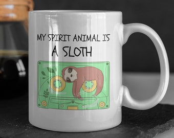 May include: White ceramic mug featuring a green cassette tape design. The tape contains a brown sloth and the text "My spirit animal is a sloth".