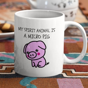 Pode incluir: Caneca de cerâmica branca com um porco rosa de desenho animado e o texto "Meu animal espiritual é um micro porco".