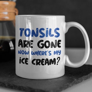 Pode incluir: Caneca de cerâmica branca com um gráfico azul e preto que diz "Tonsils are gone now where's my ice cream?"