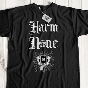 May include: Black t-shirt with white text that reads "Harm None" in a gothic font. A hand holding three tarot cards with a pentagram symbol is below the text.