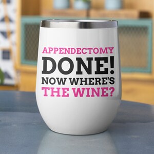May include: White stainless steel wine tumbler with black text that reads "Appendicectomy Done! Now Where's The Wine?" The text "Done!" is in pink.