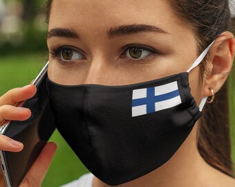 May include: A woman wearing a black face mask with the Finnish flag on it, talking on a cell phone.