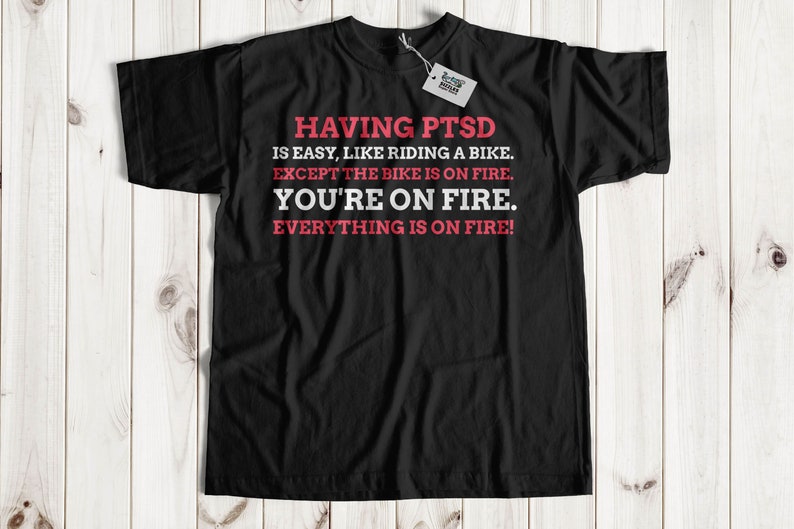 May include: Black t-shirt with red text that reads "HAVING PTSD IS EASY, LIKE RIDING A BIKE. EXCEPT THE BIKE IS ON FIRE. YOU'RE ON FIRE. EVERYTHING IS ON FIRE!"