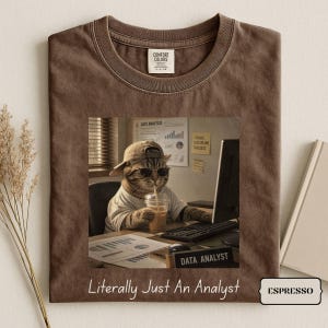 May include: A brown t-shirt featuring a graphic of a cat wearing a baseball cap and sunglasses while working at a computer with a drink. The graphic includes charts and text reading Data Analysis and Data Analyst. The shirt text reads Literally Just An Analyst.