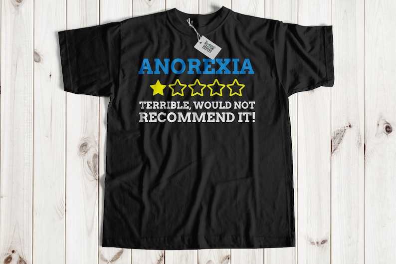 May include: Black t-shirt with a blue and white graphic that says "ANOREXIA" with five yellow stars and the text "TERRIBLE, WOULD NOT RECOMMEND IT!"