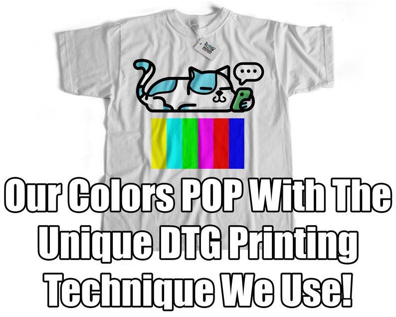 May include: White t-shirt featuring a cartoon cat with blue and white accents, holding a phone. Below the cat is a colorful test pattern. The shirt has the text "Our Colors POP With The UNIQUE DTG Printing Technique We Use!"