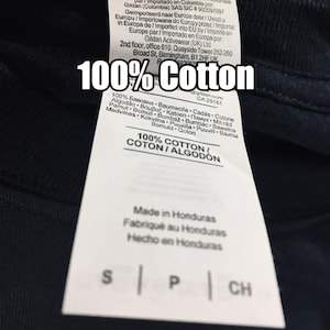 Puede incluir: Una etiqueta blanca con texto negro en una camiseta azul marino. La etiqueta dice "100% Algod&oacute;n" y enumera la composici&oacute;n de la tela en varios idiomas. Tambi&eacute;n dice "Hecho en Honduras" e incluye las tallas: S, P y CH.