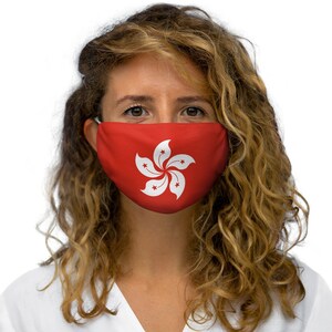 Op de afbeelding: Een vrouw draagt ​​een rood gezichtsmasker met een wit gestileerd bloemendesign, dat de vlag van Hongkong voorstelt.