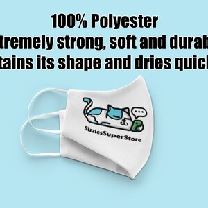 Op de afbeelding: Witte gezichtsmasker met een cartoon-kattenontwerp en de tekst "Sizzles SuperStore". Het masker is gemaakt van 100% polyester en wordt beschreven als extreem sterk, zacht, duurzaam, behoudt zijn vorm en droogt snel.