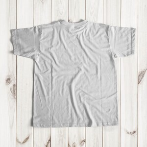 May include: A white t-shirt laid flat on a light wood surface.