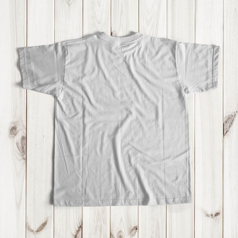 May include: A white t-shirt laid flat on a light wood surface.