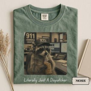 Könnte beinhalten: Ein moosgrünes T-Shirt mit einer Grafik eines Waschbären, der eine 911 Dispatcher-Kappe und eine Sonnenbrille trägt und ein Getränk sowie ein Headset hält. Im Hintergrund steht 911 Dispatch Center, darunter der Text Literally Just A Dispatcher.
