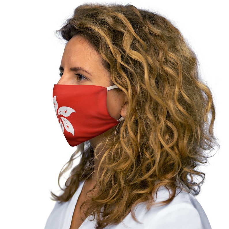 Op de afbeelding: Een vrouw draagt ​​een rood gezichtsmasker met een wit Hong Kong-vlagontwerp. Het masker heeft witte elastische banden.