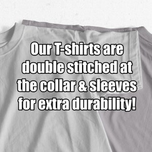 Puede incluir: Primer plano de dos camisetas grises dobladas juntas. El texto "Our T-shirts are double stitched at the collar & sleeves for extra durability!" est&aacute; impreso en las camisetas.