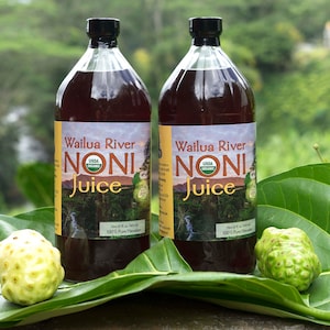 May include: Two glass bottles of dark red noni juice with a green label that says "Wailua River Noni Juice" and a USDA Organic seal. The bottles are sitting on green leaves with two green noni fruits.