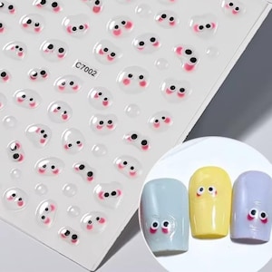 May include: Sheet of nail art stickers featuring cartoon eyes with black pupils and pink cheeks. The stickers are clear with a 3D effect. The sheet also includes three painted nails with cartoon eye designs.