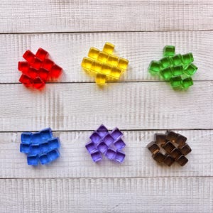 May include: Six clusters of small, translucent, square-shaped glass cubes arranged in groups of red, yellow, green, blue, purple, and brown. Each cluster contains multiple individual cubes with smooth, reflective surfaces and rounded edges.
