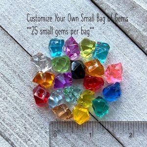 May include: A collection of colorful, faceted gems in various colors, including blue, pink, yellow, and orange. The text "Customize Your Own Small Bag of Gems" and "25 small gems per bag" is visible. A ruler shows the gems are approximately 1 inch in size.