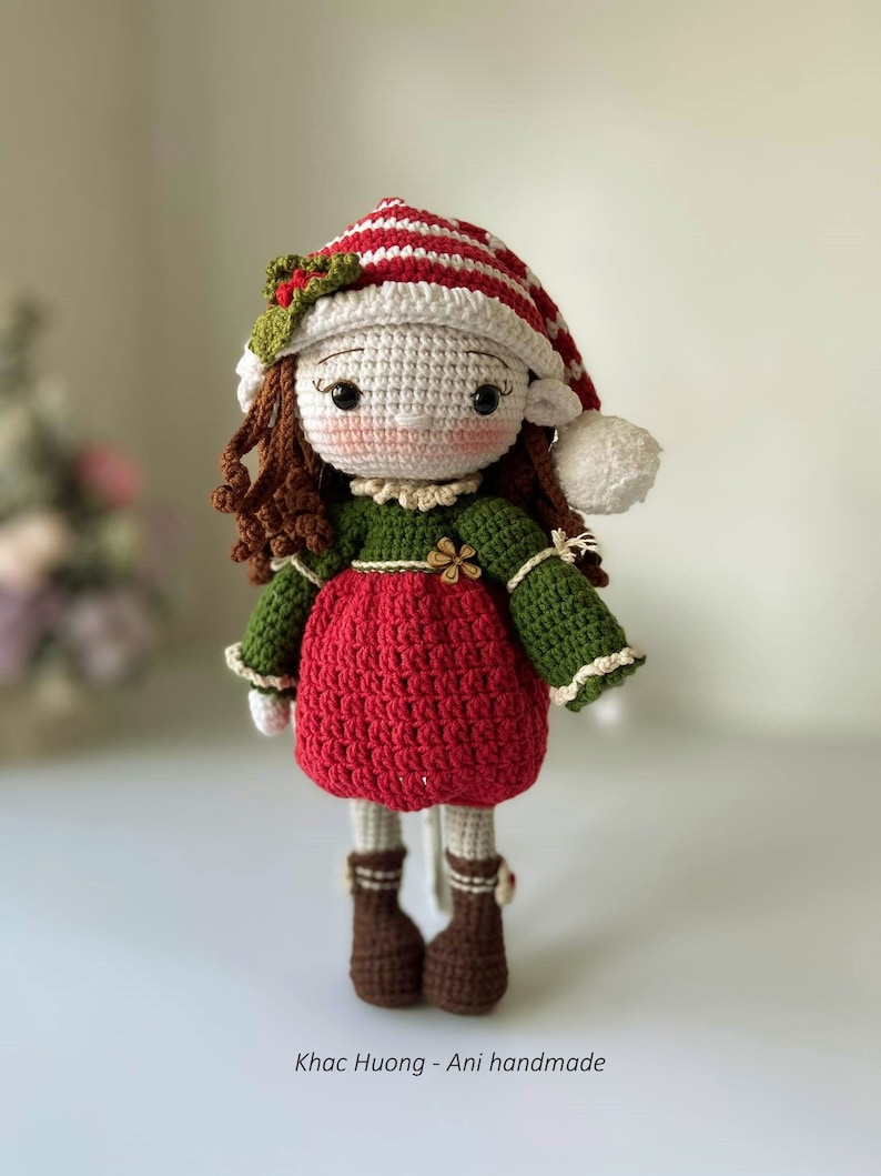 May include: A crocheted doll wearing a red and white striped hat with a green sweater and red dress. The doll has brown hair and brown boots.