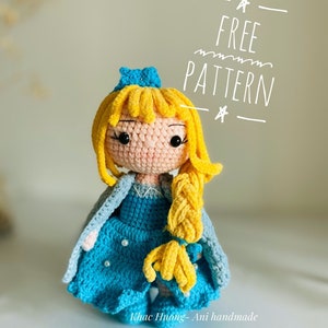 May include: A crocheted doll with long blonde hair, wearing a blue dress and a blue cape. The doll has a crown on its head and is holding a braid of hair. The text "FREE PATTERN" is written above the doll.