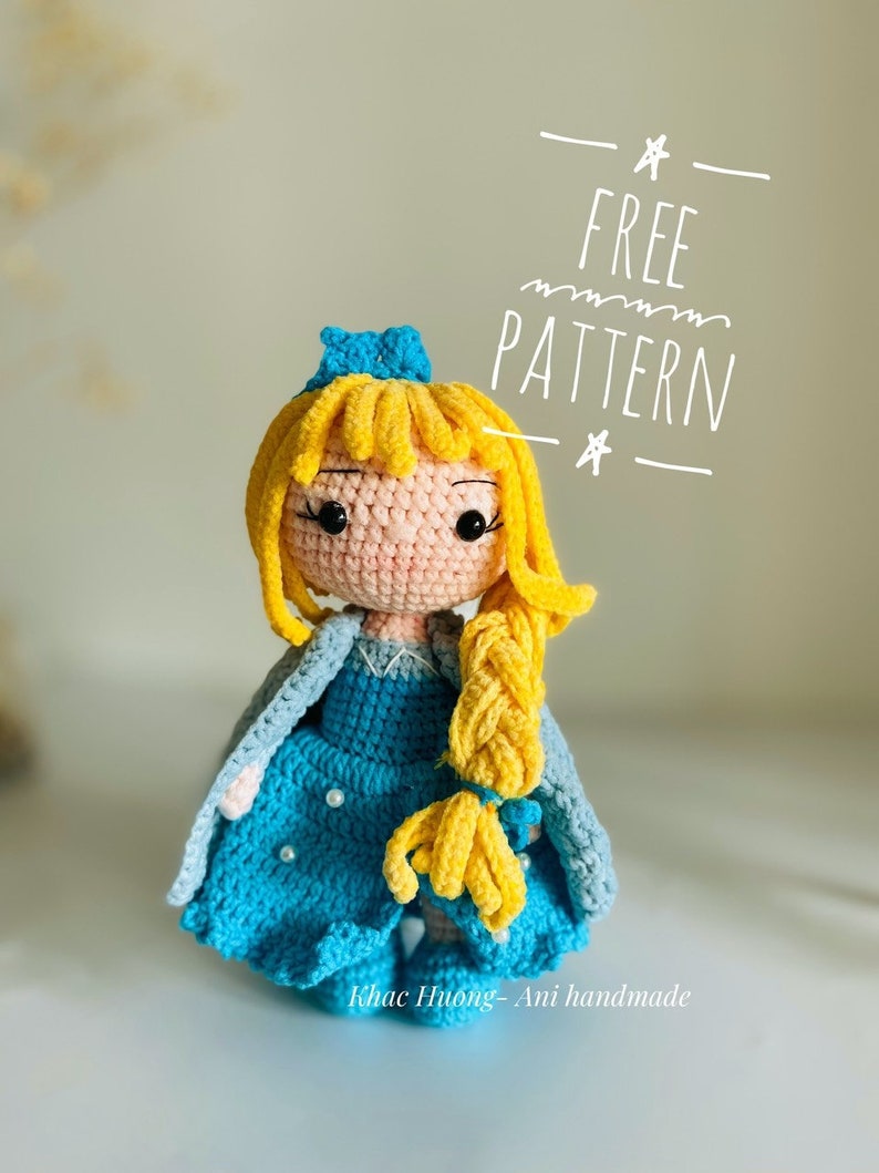 May include: A crocheted doll with long blonde hair, wearing a blue dress and a blue cape. The doll has a crown on its head and is holding a braid of hair. The text "FREE PATTERN" is written above the doll.