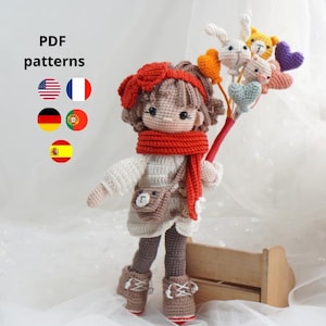 Puede incluir: Una muñeca de ganchillo hecha a mano con una bufanda, diadema y botas rojas. La muñeca sostiene un ramo de animales y corazones de ganchillo. La imagen incluye el texto "PDF patterns" y banderas de diferentes países.