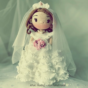 Puede incluir: Una mu&ntilde;eca de crochet vestida con un vestido de novia blanco con velo y sosteniendo un ramo de flores rosas. La mu&ntilde;eca tiene el pelo casta&ntilde;o y una corona.