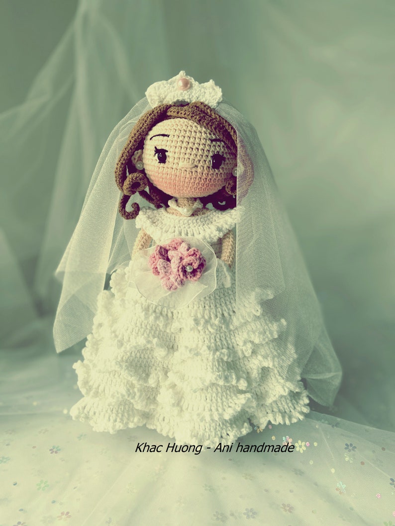 Puede incluir: Una mu&ntilde;eca de crochet vestida con un vestido de novia blanco con velo y sosteniendo un ramo de flores rosas. La mu&ntilde;eca tiene el pelo casta&ntilde;o y una corona.