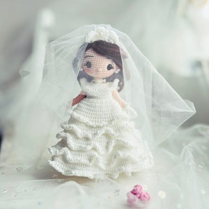 Puede incluir: Una mu&ntilde;eca de crochet vestida con un vestido de novia blanco con velo. La mu&ntilde;eca tiene el pelo casta&ntilde;o y una flor blanca en la cabeza.