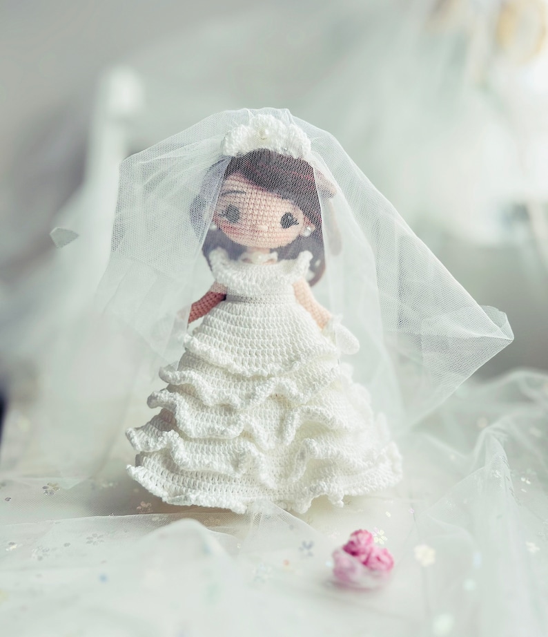 Puede incluir: Una mu&ntilde;eca de crochet vestida con un vestido de novia blanco con velo. La mu&ntilde;eca tiene el pelo casta&ntilde;o y una flor blanca en la cabeza.