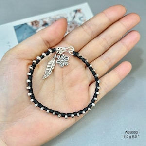 May include: Black cord bracelet with silver-tone details and charms. The bracelet has a feather and flower charm. The bracelet is 16.5 cm long and weighs 8.0 grams.