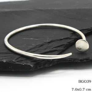 May include: A silver-colored open cuff bracelet with a rounded ball accent. The bracelet is approximately 7.0 cm in diameter and 0.7 cm wide. The bracelet is displayed on a dark, textured surface. The product code is BGO39.