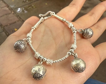 May include: A silver bracelet with four dangling bell charms. The bracelet features a hook clasp and is composed of small beads and decorative elements. The bell charms have intricate patterns and a spherical shape.