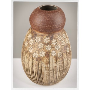May include: A brown and beige ceramic vase with a textured surface and white flower designs. The vase has a rounded body and a wide opening.