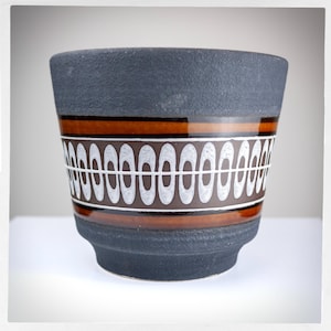 Peut inclure: Un pot en céramique noir avec un motif géométrique brun et blanc. Le pot a une surface texturée et une forme arrondie.
