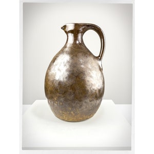 May include: A brown ceramic jug with a wide mouth and a handle. The jug has a speckled glaze with a metallic sheen.