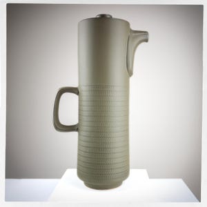 May include: A tall, green ceramic jug with a textured, ribbed design. The jug has a spout and a handle.