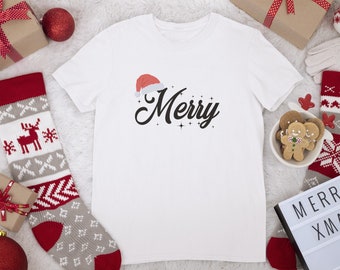 May include: White t-shirt featuring a red Santa hat and the word "Merry" in black script. The shirt is surrounded by Christmas decorations, including a stocking, a gift box, and a light-up sign that reads "Merry Xmas".