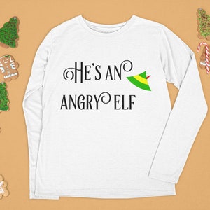 May include: White long-sleeved t-shirt with the text "He's an Angry Elf" and a green elf hat graphic.