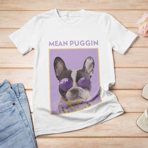 May include: White t-shirt with a purple and yellow graphic of a French bulldog wearing sunglasses and the text "MEAN PUGGIN".