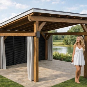 May include: A wooden pergola with a flat roof, supported by thick, brown posts. The structure has grey curtains and a black slatted wall. A woman in a white dress stands nearby on a stone patio, with a lake and trees in the background.