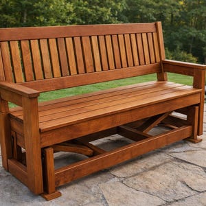 May include: A wooden outdoor glider bench with a slatted back and armrests. The bench is made of stained wood and has a natural finish. The bench is designed for outdoor use and is placed on a stone patio.