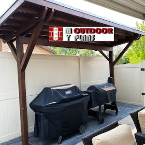 May include: A wooden pergola with a dark brown stain and a corrugated metal roof. Two black grill covers are visible beneath the pergola. The text "M Outdoor Plans" is displayed on a white background.
