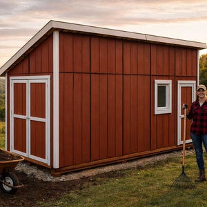 Pode incluir: Um galpão de madeira vermelho com acabamentos brancos e um telhado branco. Uma pessoa está ao lado do galpão segurando um ancinho. Um carrinho de mão e uma pá estão em frente ao galpão.