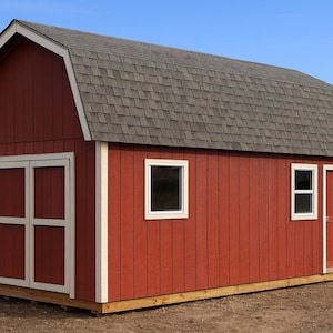 May include: A red barn-style shed with a gray shingled roof. The shed has white-framed windows and doors. The doors are double doors. The shed is on a wooden foundation and set against a blue sky.