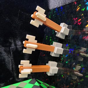 May include: Three toy-like objects with a brown central beam, white accents, and grey bases. They are arranged diagonally against a black and iridescent background. The design suggests a playful or artistic theme.